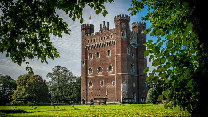 Tattershall Castle's Great Tower surrounded by blue sky and bright green leaves on branches are seen near the edges of the picture